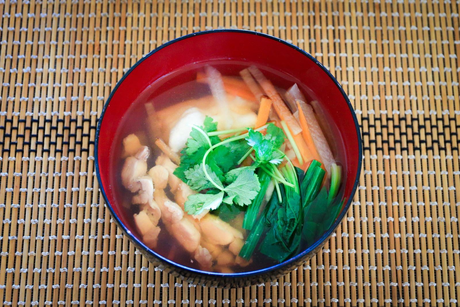 竹すだれの上に置かれた赤い漆椀に入った三つ葉や鶏肉が入った澄まし雑煮
