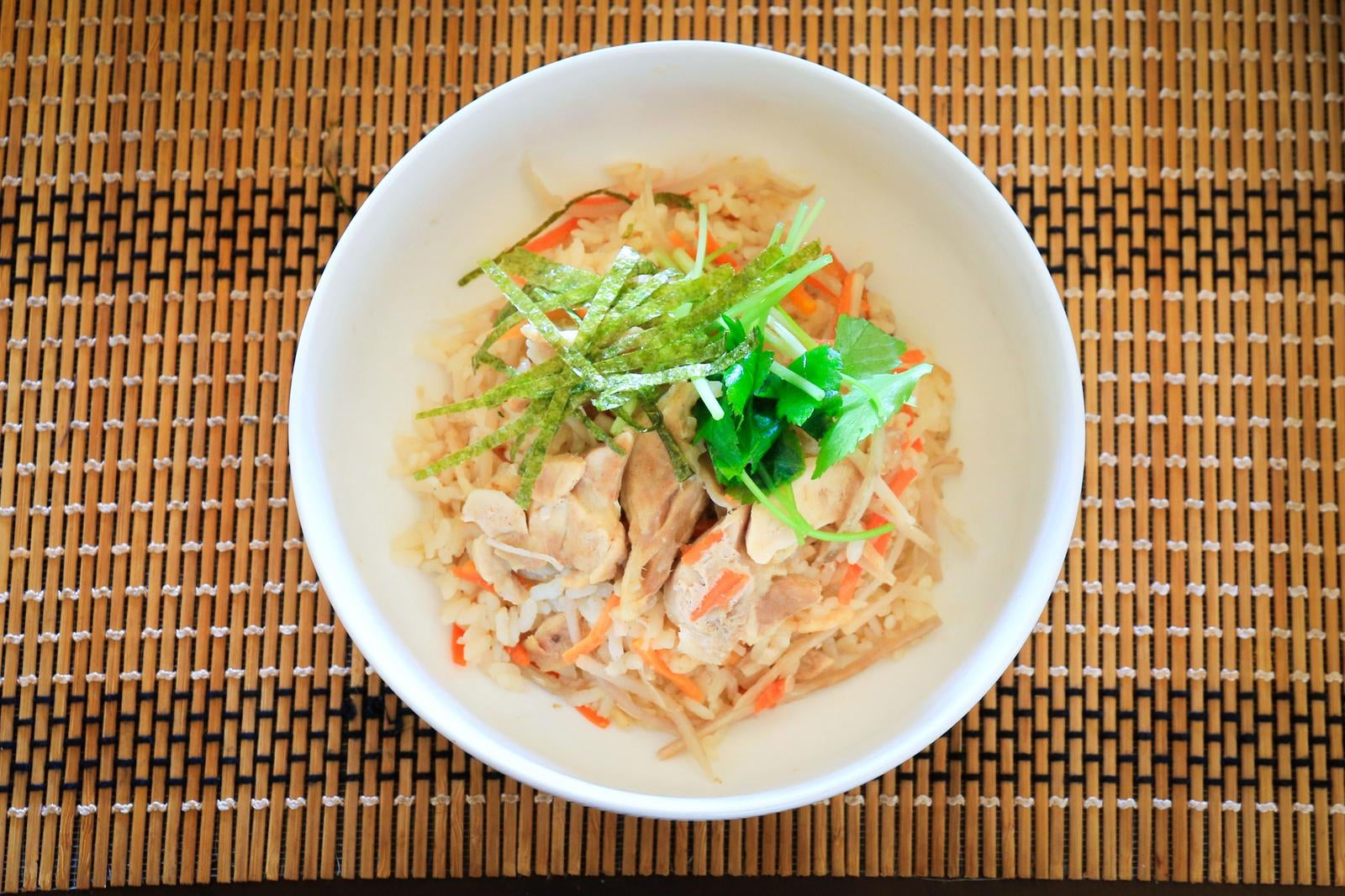 竹すだれの上に置かれた白い茶碗に盛られた鶏めし（炊き込みご飯）を真上から撮影した写真
