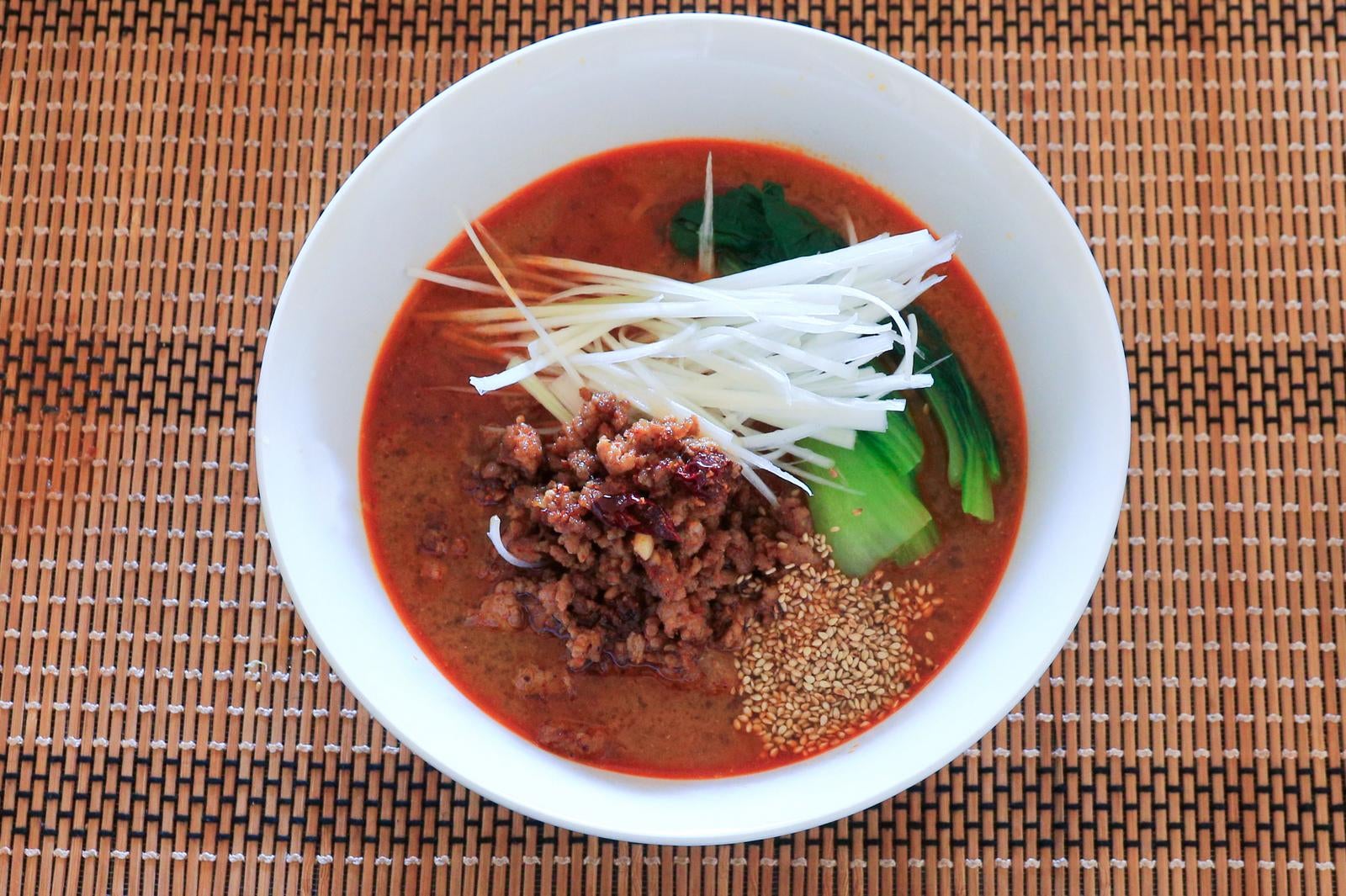 竹のランチョンマットの上に置かれた肉味噌と白髪ねぎがのった担々麺を真上から撮影