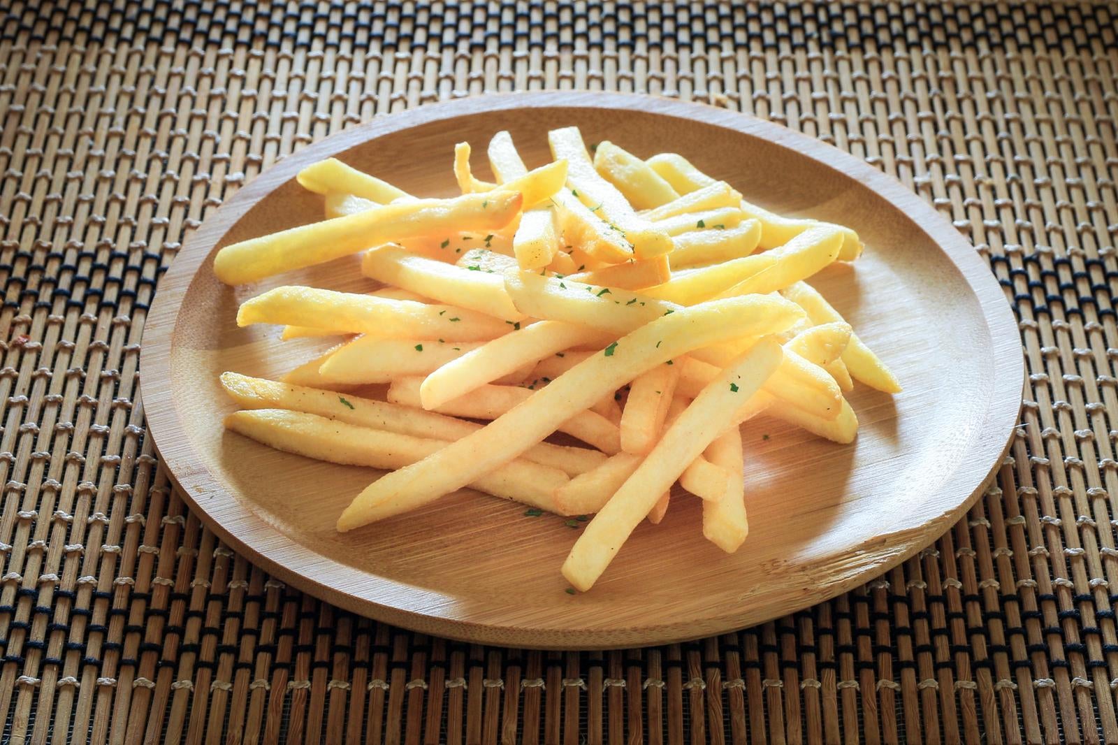 竹製ランチョンマットの上に置かれた木皿に盛られたパセリ付きフライドポテト