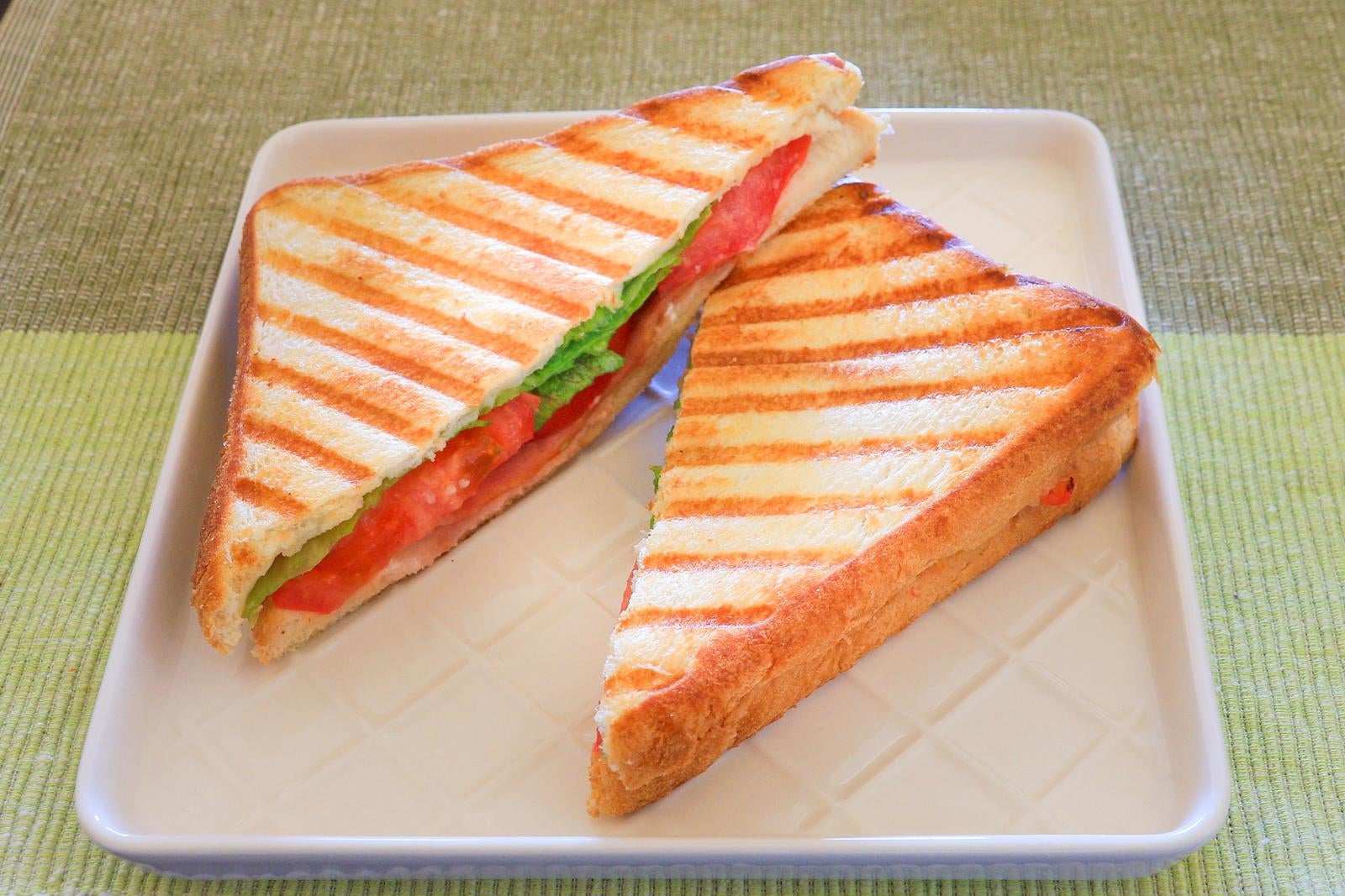 白い皿に盛られたトマトとレタス入りのホットサンド2切れ