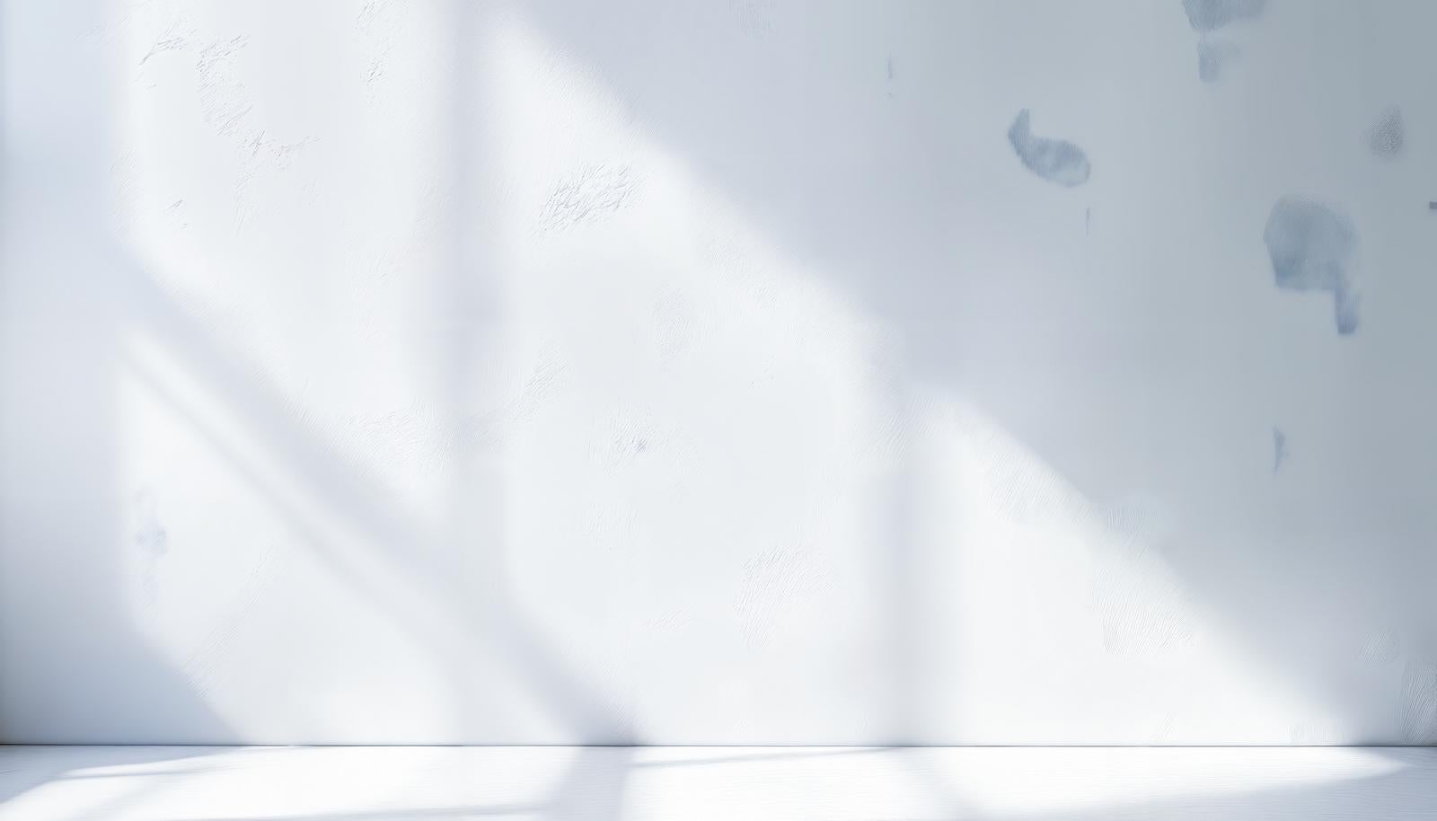 Simple background with natural light from a window casting diagonal shadows on a white plaster-textured wall