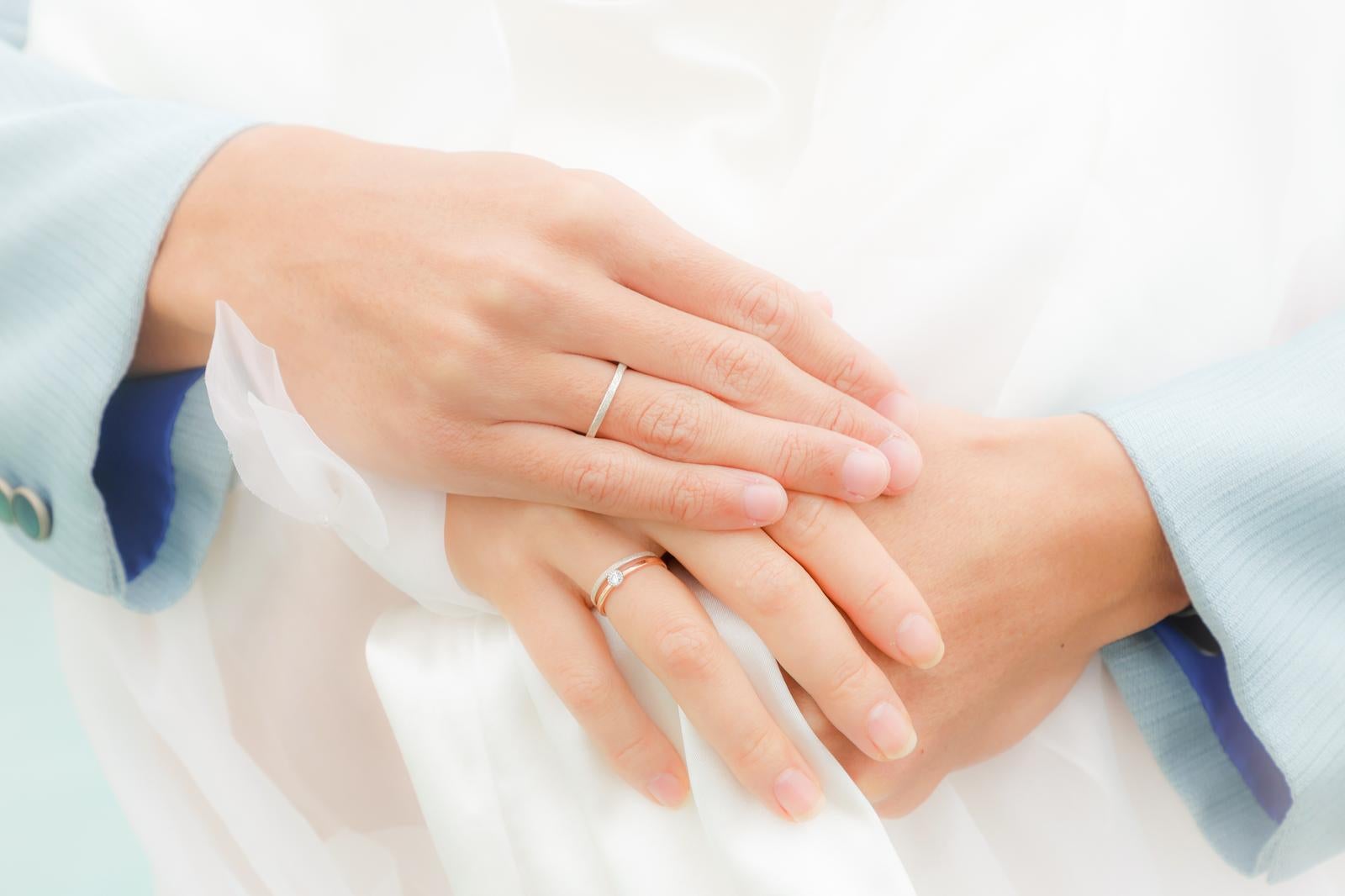 Newlyweds wearing engagement rings and wedding rings clasping hands together over a white dress