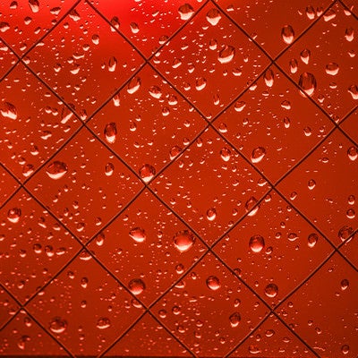 赤く染まる外と窓の水滴の写真