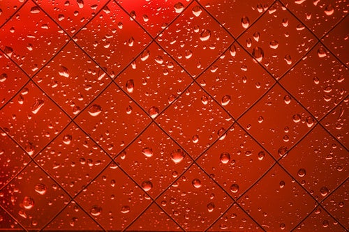 赤く染まる外と窓の水滴の写真