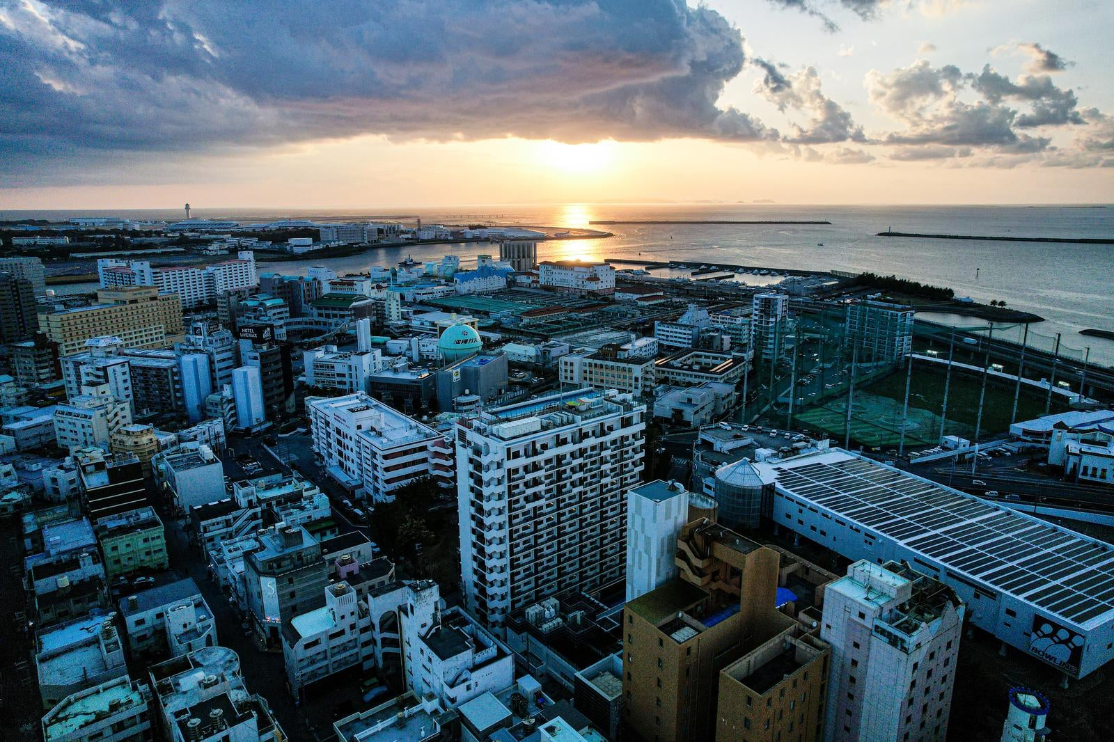 Landscape photograph of a coastal cityscape taken from above at dusk, with sunset (Yuuhi) illuminating the sea surface