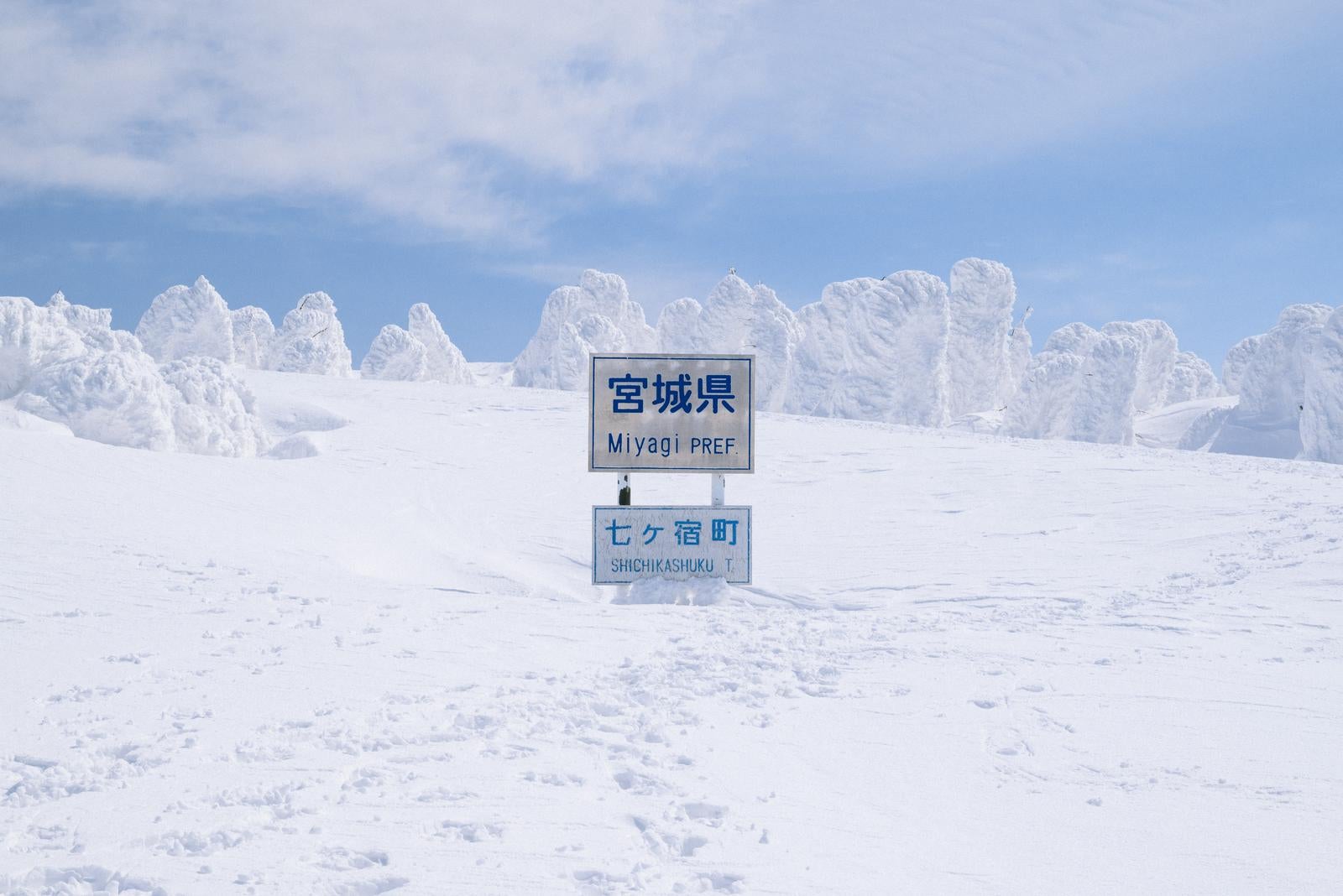 「雪に覆われた宮城県県境の看板と足跡」の写真