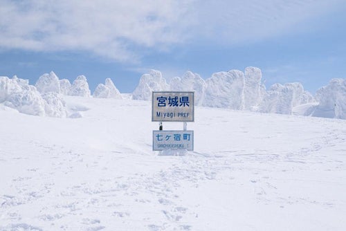 雪に覆われた宮城県県境の看板と足跡の写真