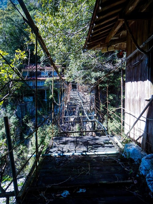 廃墟となった旅館へ続くボロボロの吊り橋の写真