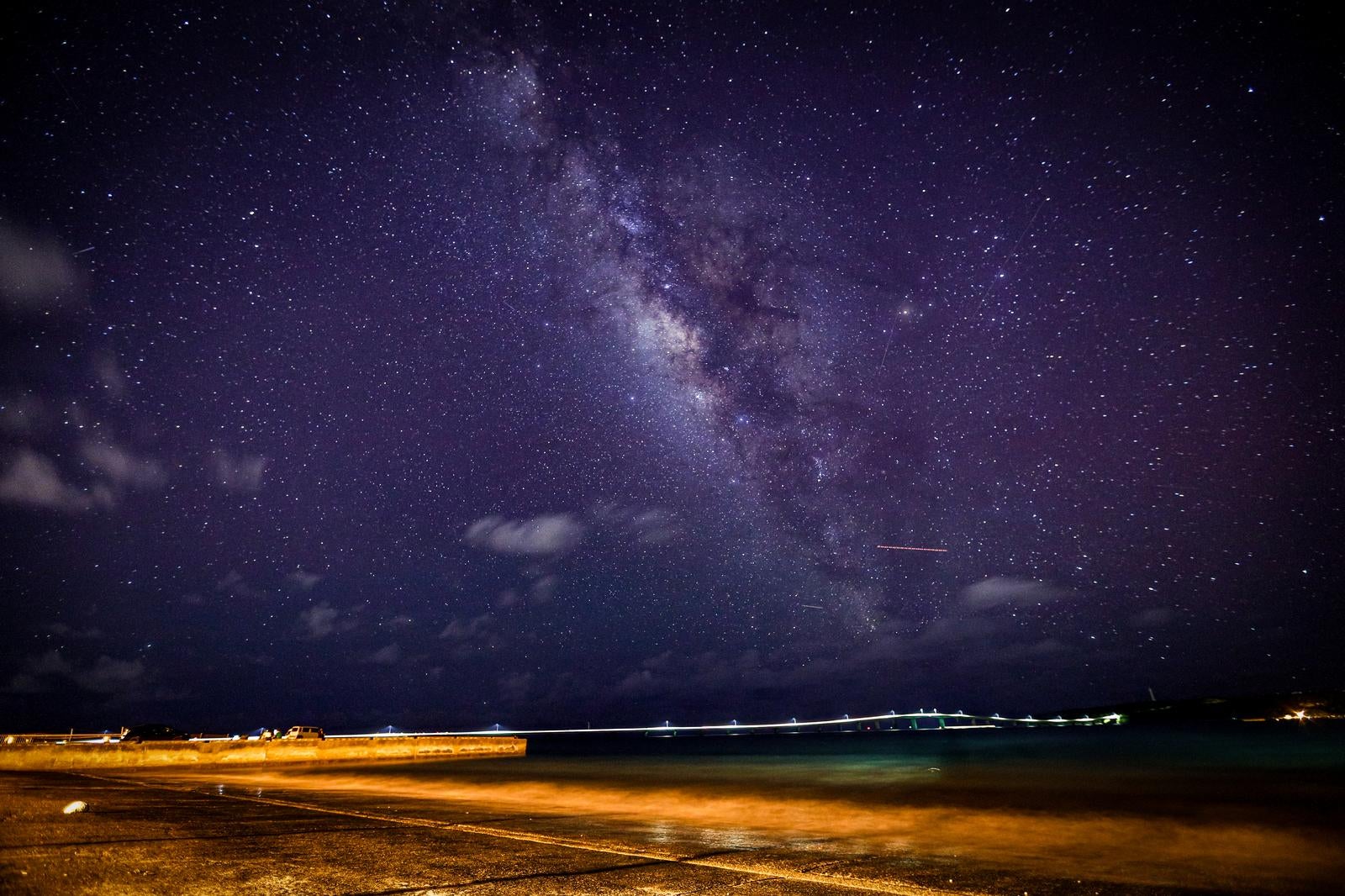 海辺の堤防から見上げた天の川が夜空に広がる星空の風景写真