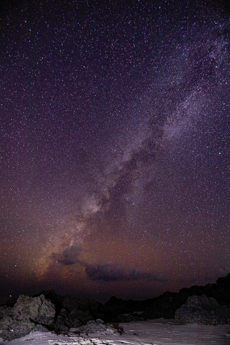 岩場のシルエットの上に天の川が縦に伸びる満天の星空の夜景