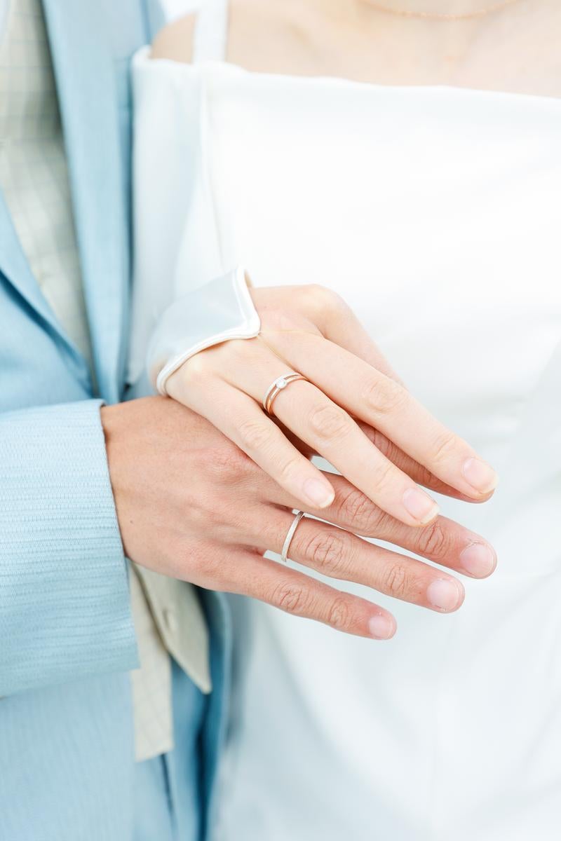 水色のジャケットを着た女性が細い指輪を重ね付けした左手のクローズアップ