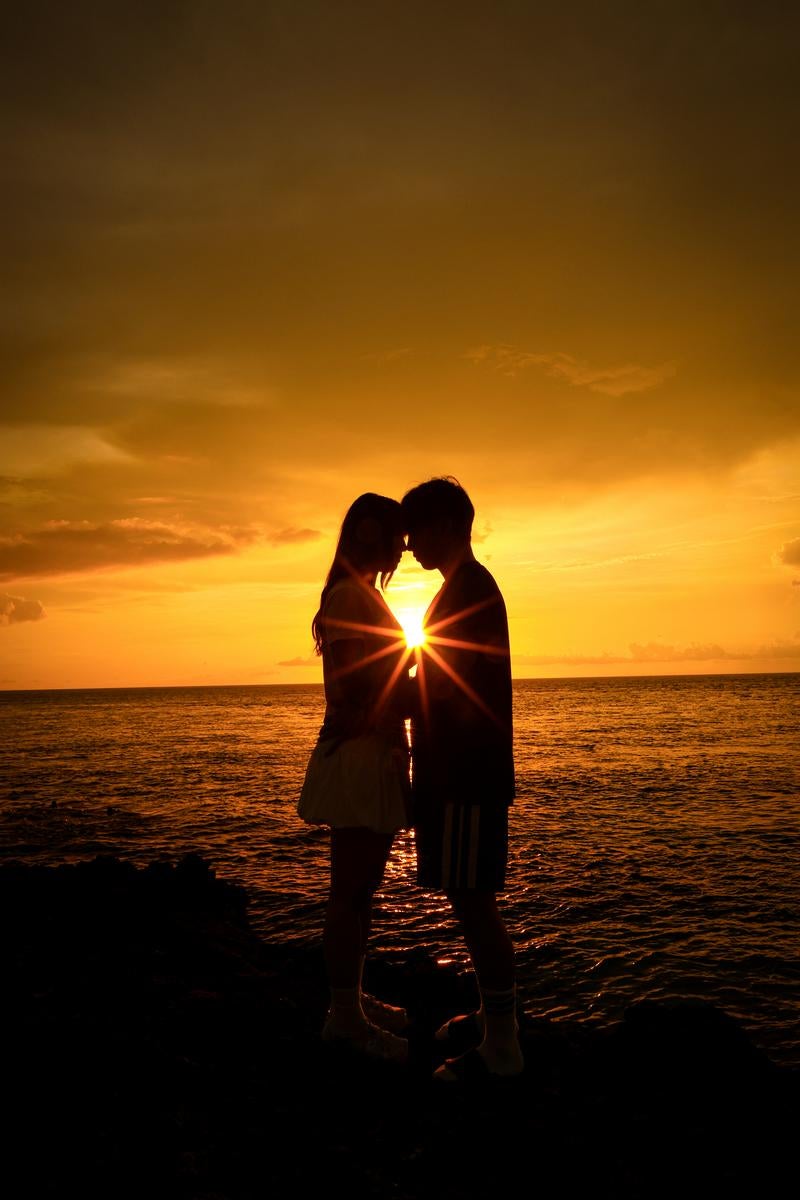 Silhouette of a couple facing each other and touching foreheads on the beach at dusk with sun rays in the background