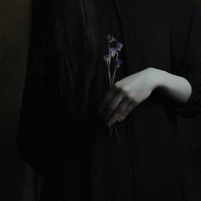 紫色の造花を持つ黒ワンピースの女性の写真