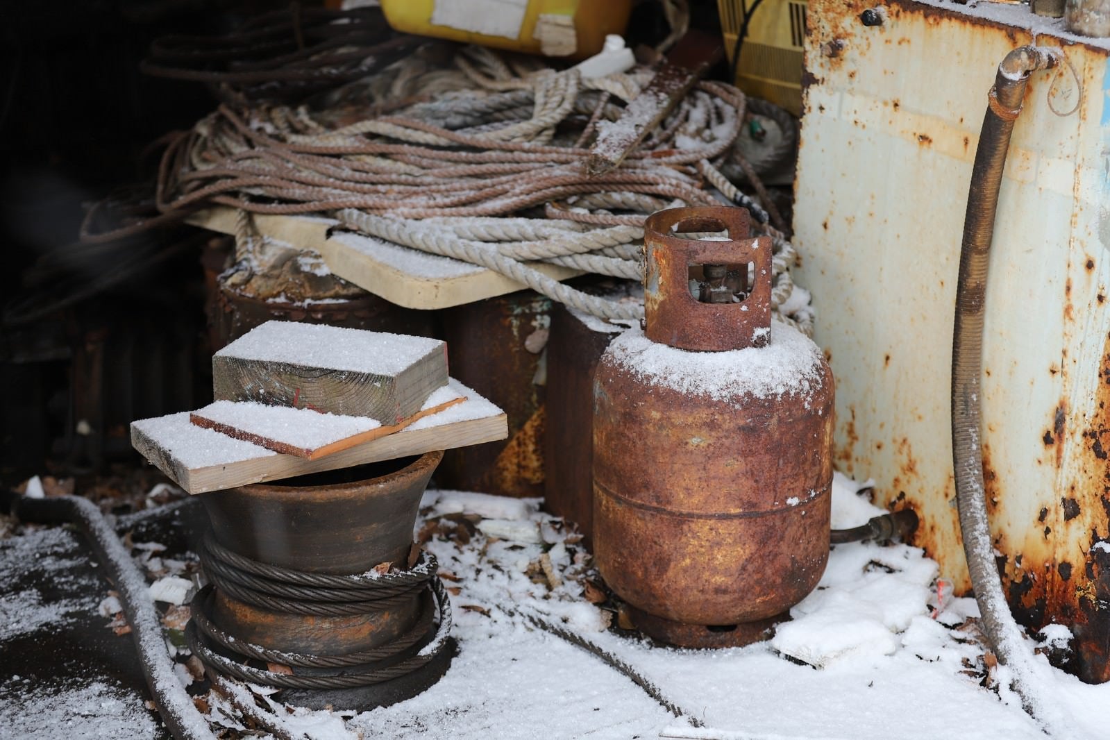 「雪の積もる錆び付くガス容器とロープ」の写真