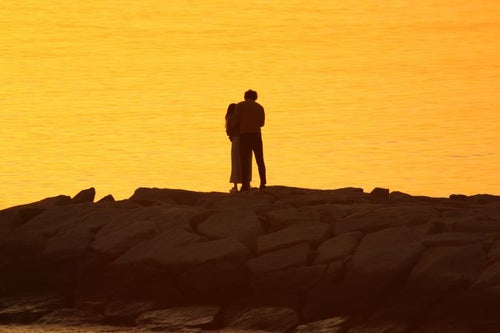夕暮れ時の海岸でいちゃつくカップルの写真