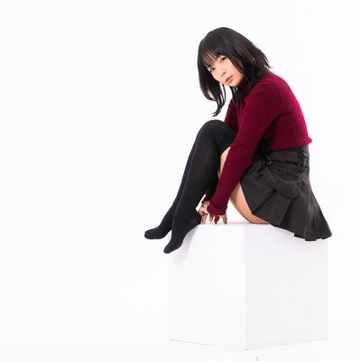 白い箱に座ってカメラを見つめる黒髪の女性の写真