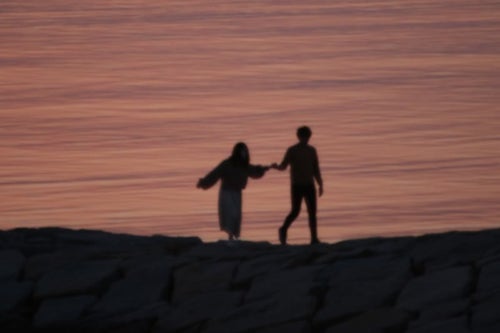 海岸で手を取るカップルのシルエットの写真