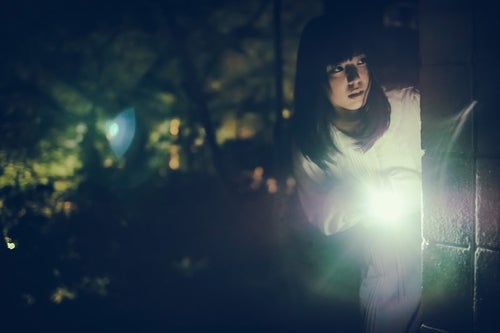 懐中電灯で辺りを警戒する女性の写真
