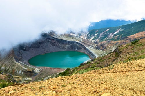 雲の合間に除くエメラルドグリーンの火山湖（蔵王山）の写真