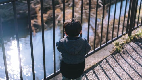 鉄柵から河川を眺める子供と散歩の写真