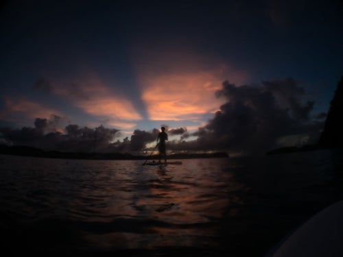夕暮れ時にイカダを漕ぐ少年のシルエットの写真