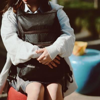 大きなリュックを抱きしめてひとやすみする女子高生の写真