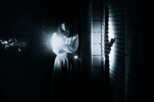 恐る恐る暗闇を歩く女性の姿の写真