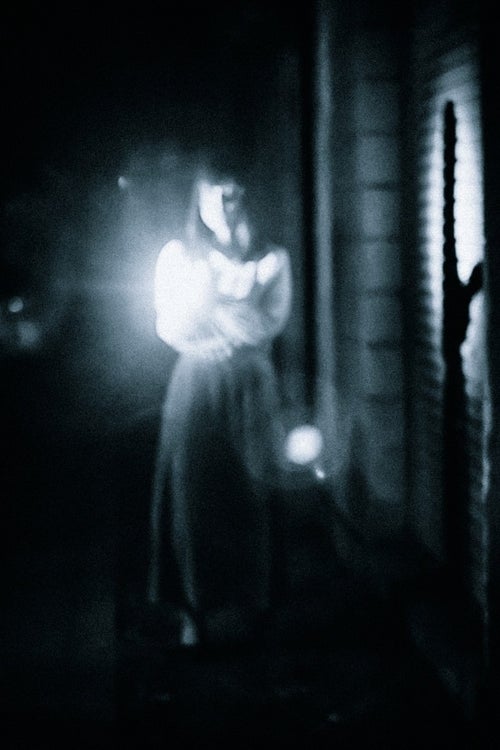 懐中電灯で正面を照らす女性の姿の写真