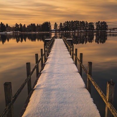 夕焼けに染まる湖面と残雪の桟橋の写真
