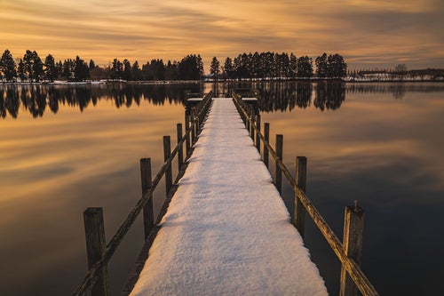 夕焼けに染まる湖面と残雪の桟橋の写真