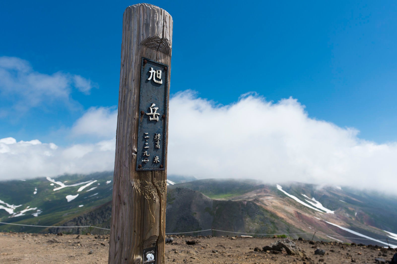 「背景に雲が流れる旭岳山頂の木碑」の写真