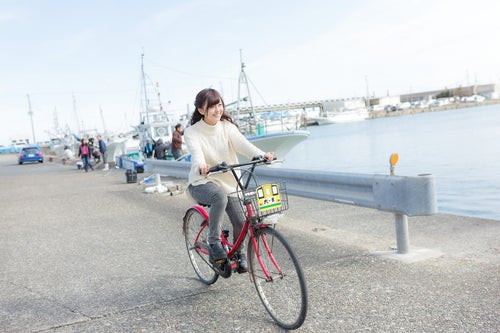レンタサイクルで漁港を走る女性観光客の写真