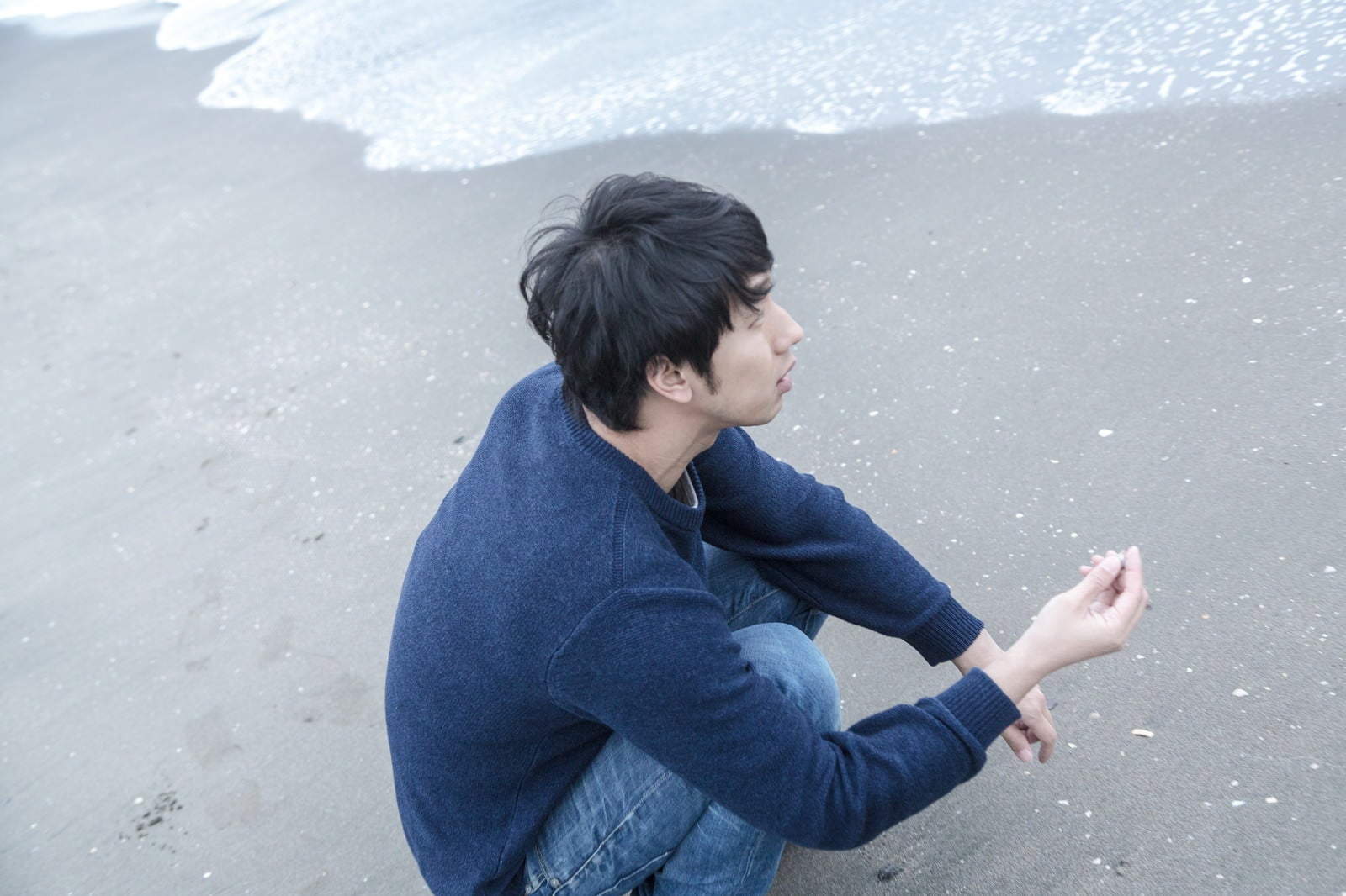 「砂浜で思いをはせる男性」の写真［モデル：大川竜弥］