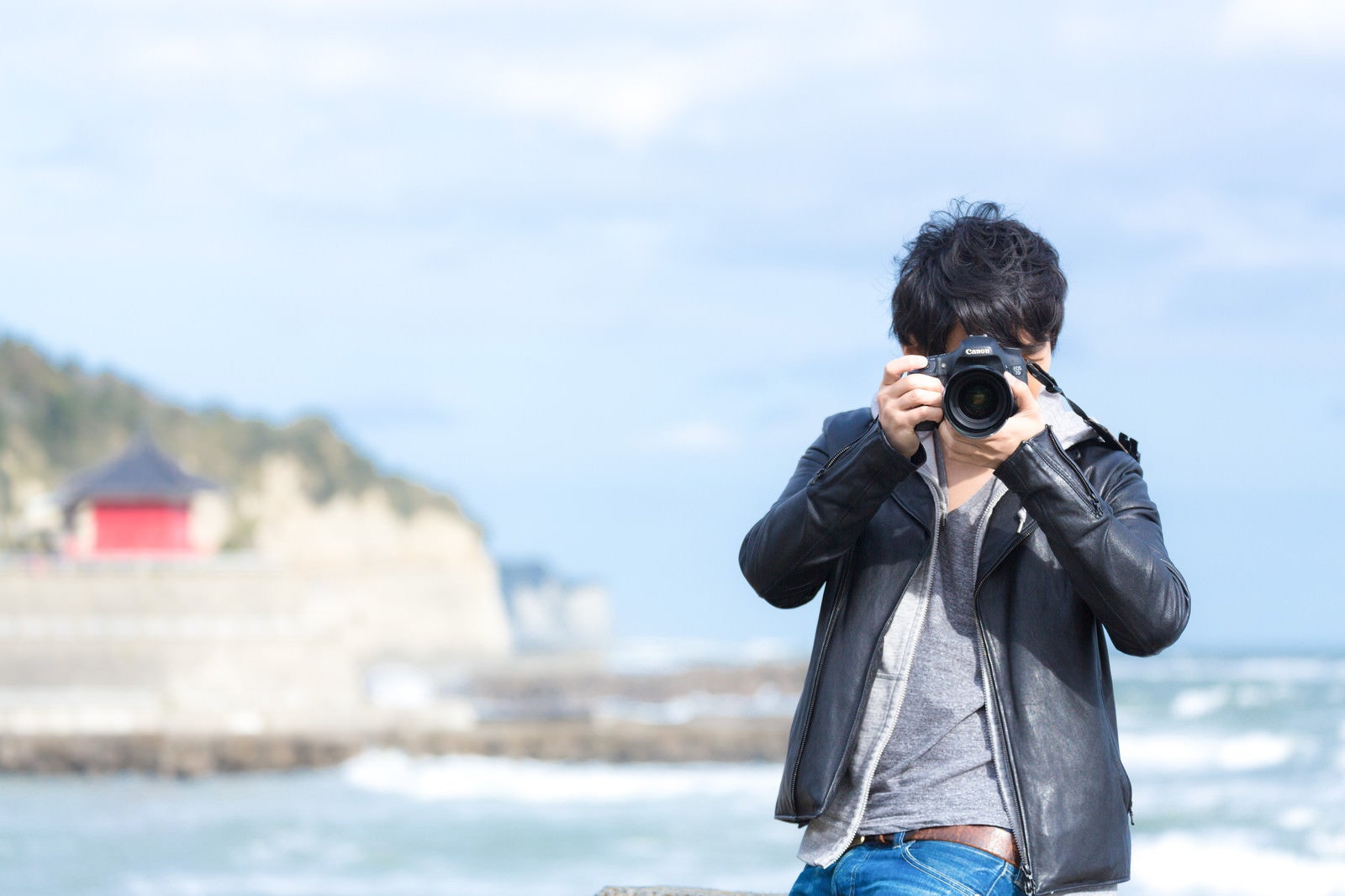 「海岸でカメラを構える男性」の写真［モデル：大川竜弥］
