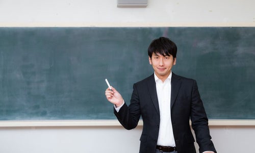 黒板の前で自己紹介をする新任教師の写真