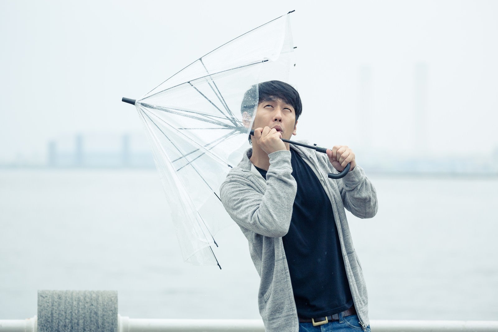 「強風で傘が持っていかれそうになる男性」の写真［モデル：大川竜弥］