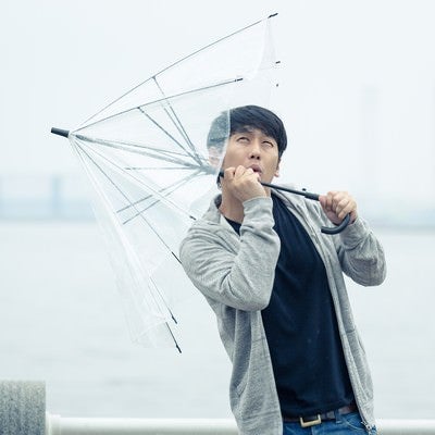 強風で傘が持っていかれそうになる男性の写真