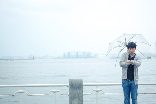 雨の日の初デート、時間を確認するしぐさで高鳴りをごまかす男性の写真