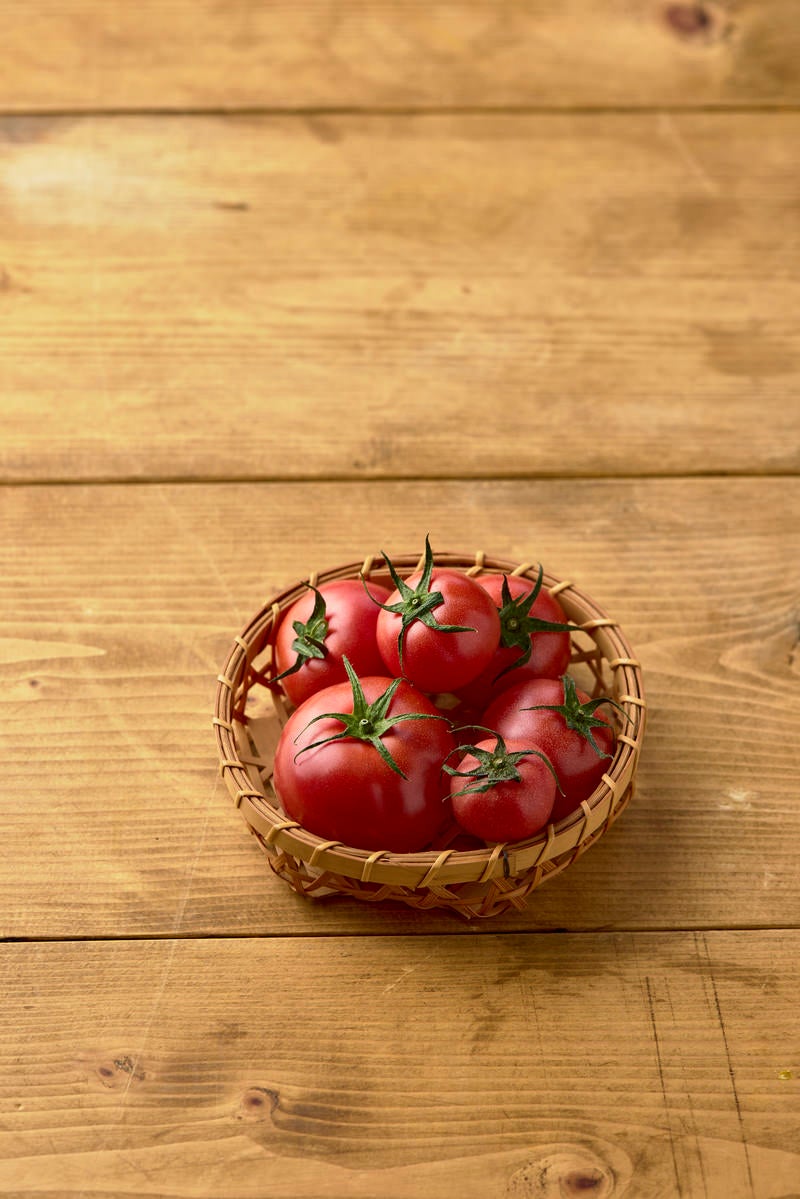 籠に入った蔕付きミニトマトの写真