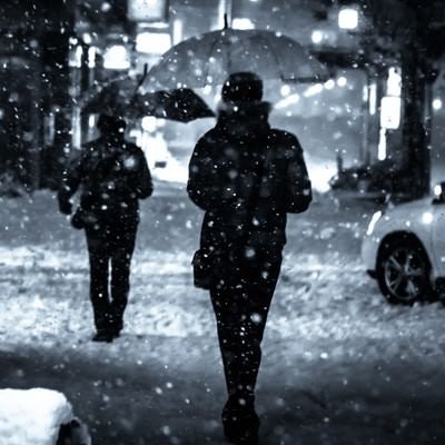 夜間、舞い散る雪と傘をさす人の写真