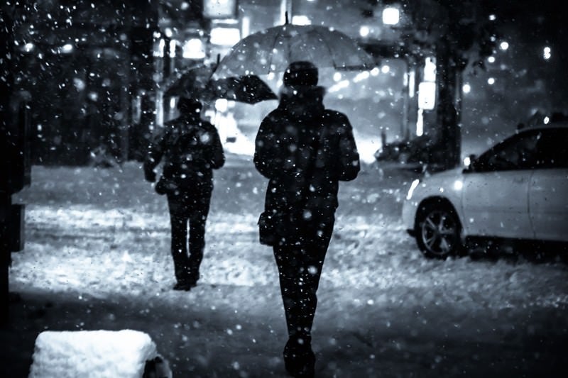 夜間、舞い散る雪と傘をさす人の写真