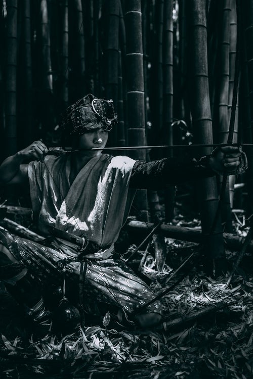 竹林の暗がりで大弓を引く野盗の写真