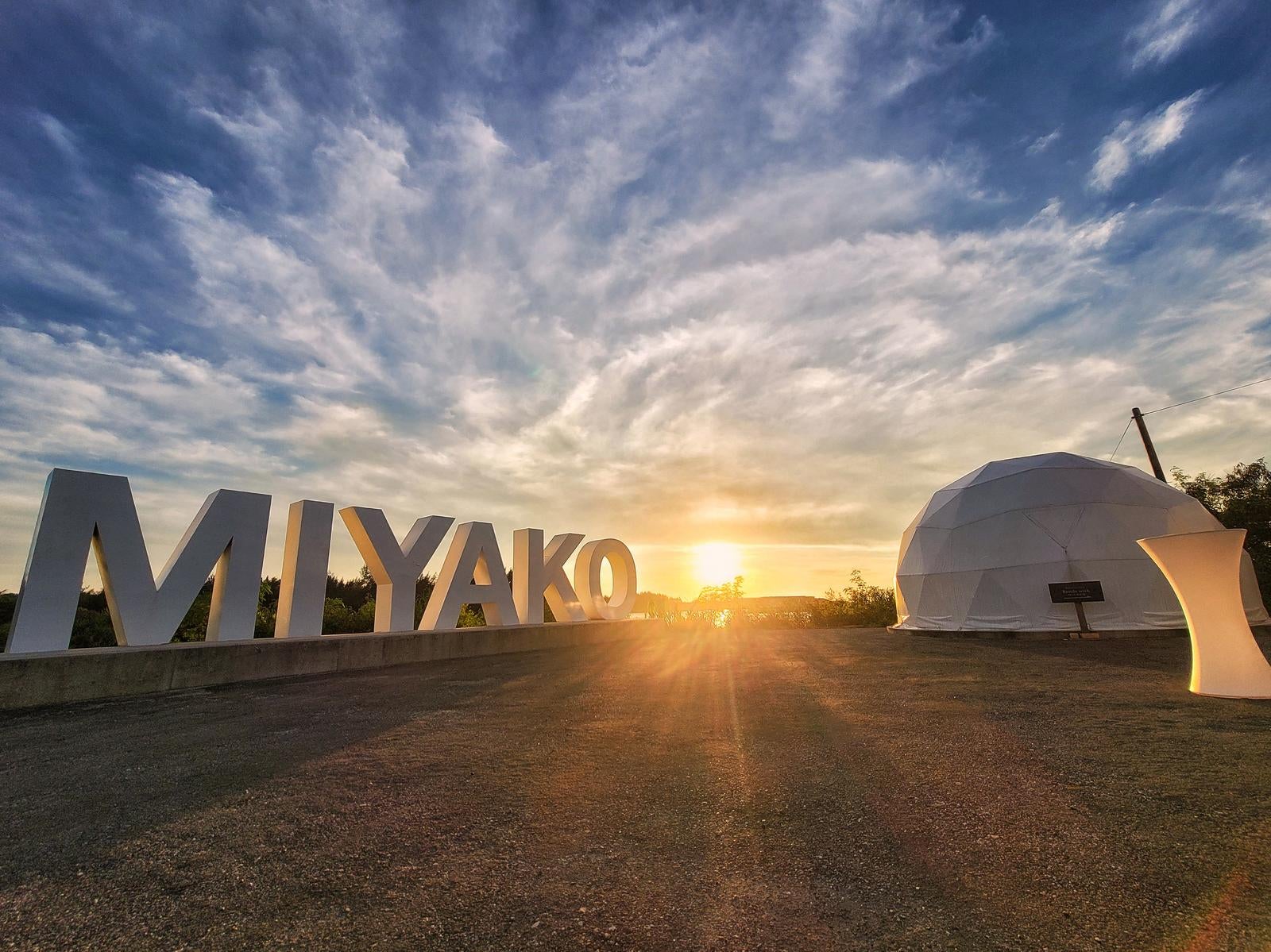 「夕陽に照らされるMIYAKOの文字とドーム型テントの風景」の写真