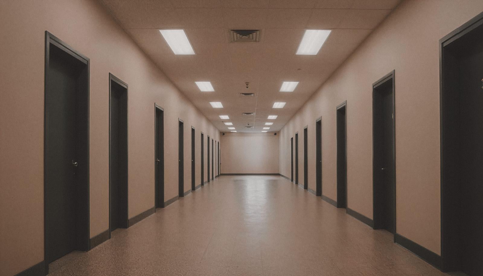 黒いドアが両側に並ぶ廊下風の通路、天井照明が続く