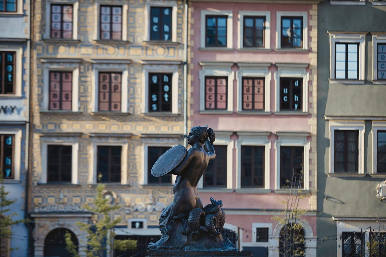 ワルシャワ旧市街広場で盾を掲げる青銅色の人魚像と背後の歴史的建築