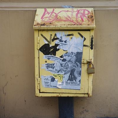 街角に残る黄色い配電盤と落書きされたステッカーの写真