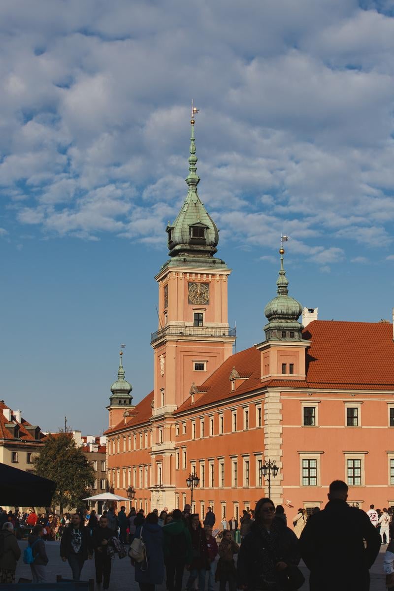 オレンジ色の王宮建築とドーム型の時計塔、観光客で賑わうワルシャワ広場