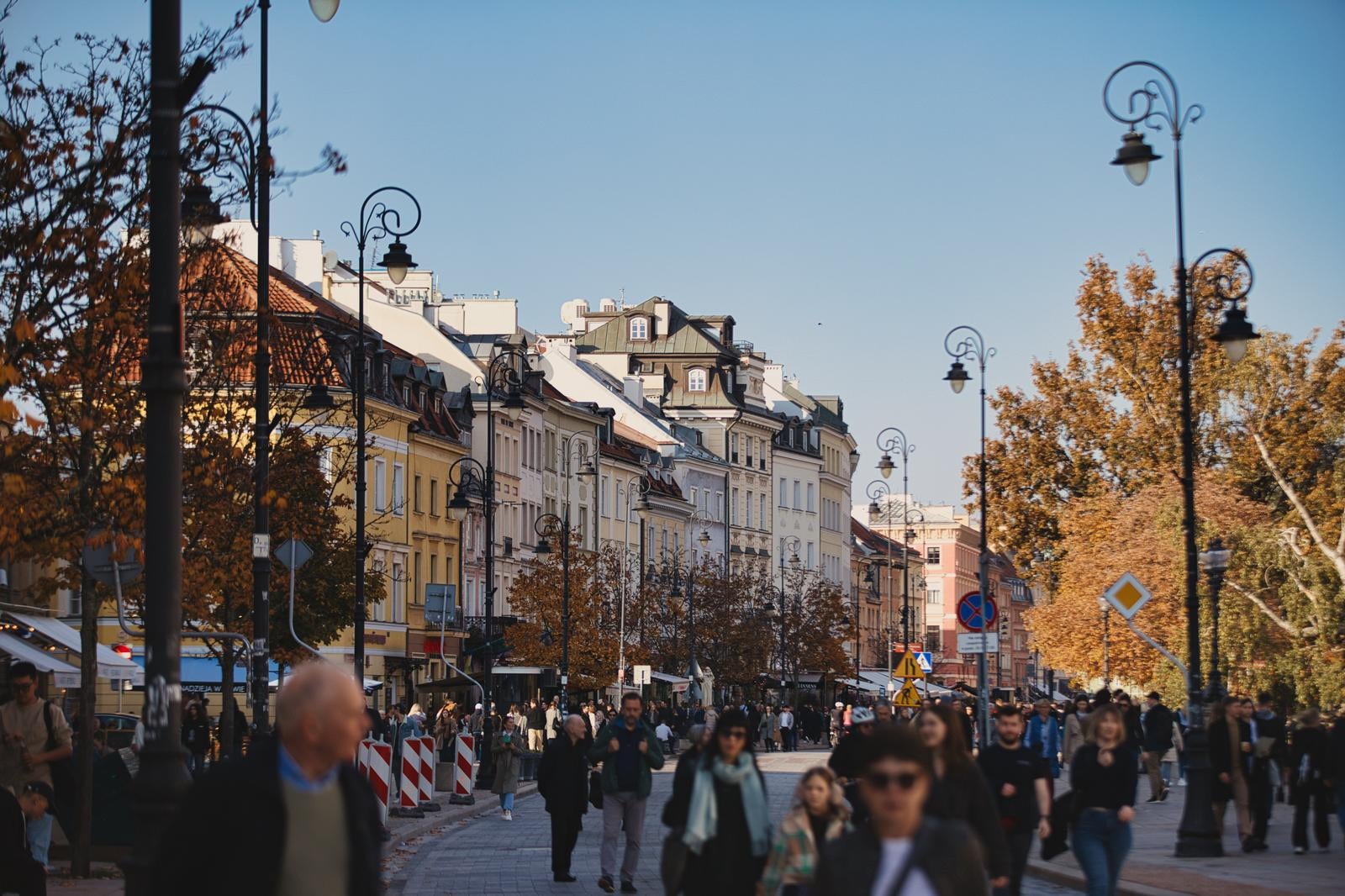 黒い街灯が並ぶワルシャワの旧市街の通りで、カラフルな建物に囲まれた広場を歩く人々