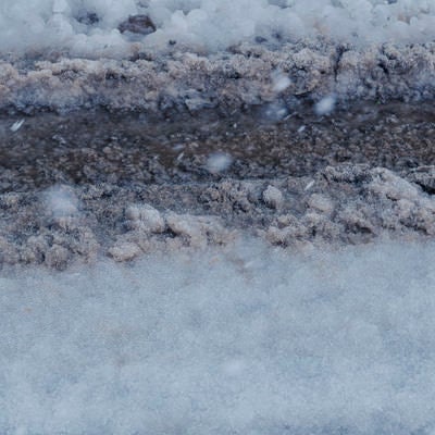 新雪と圧雪が層をなす雪道にくっきり残るタイヤ痕の写真